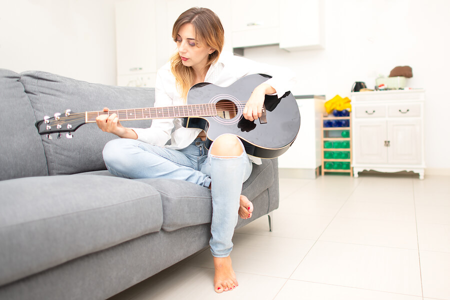 Mujer zurda sentada tocando la guitarra.